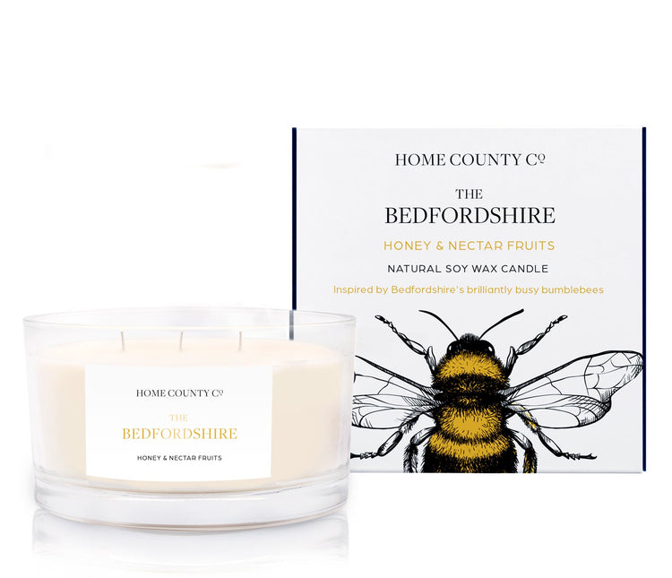 A honey and nectar fruits scented 3 wick candle from the Home County Co. is shown next to its eco-friendly candle packaging box.