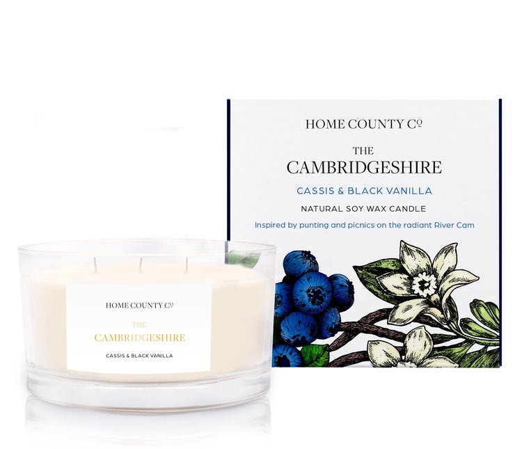 A cassis and black vanilla scented 3 wick candle from the Home County Co. is shown next to its eco-friendly candle packaging box.