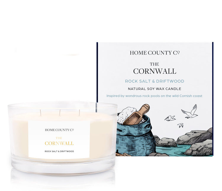 A rock salt and driftwood scented 3 wick candle from the Home County Co. is shown next to its eco-friendly candle packaging box.