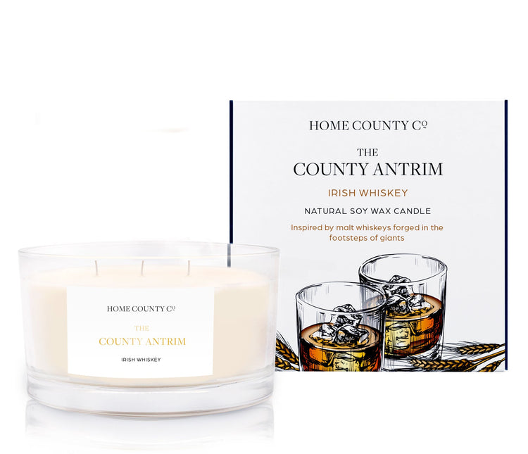 An Irish whiskey scented 3 wick candle from the Home County Co. is shown next to its eco-friendly candle packaging box.