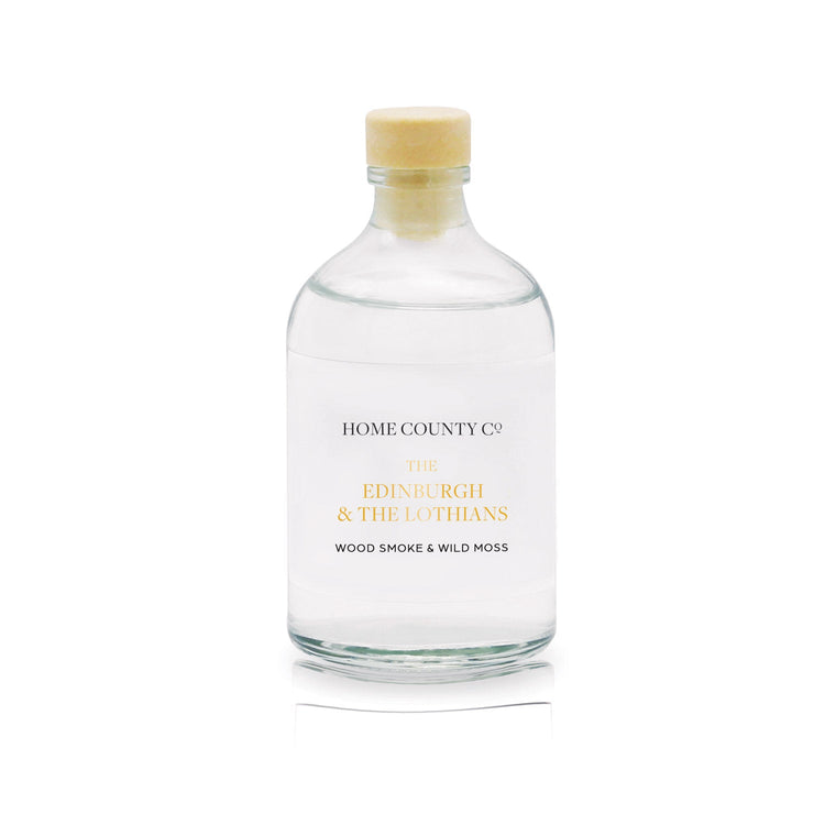 A wood smoke scented reed diffuser refill from the Home County Co is shown in its recyclable glass refill bottle.
