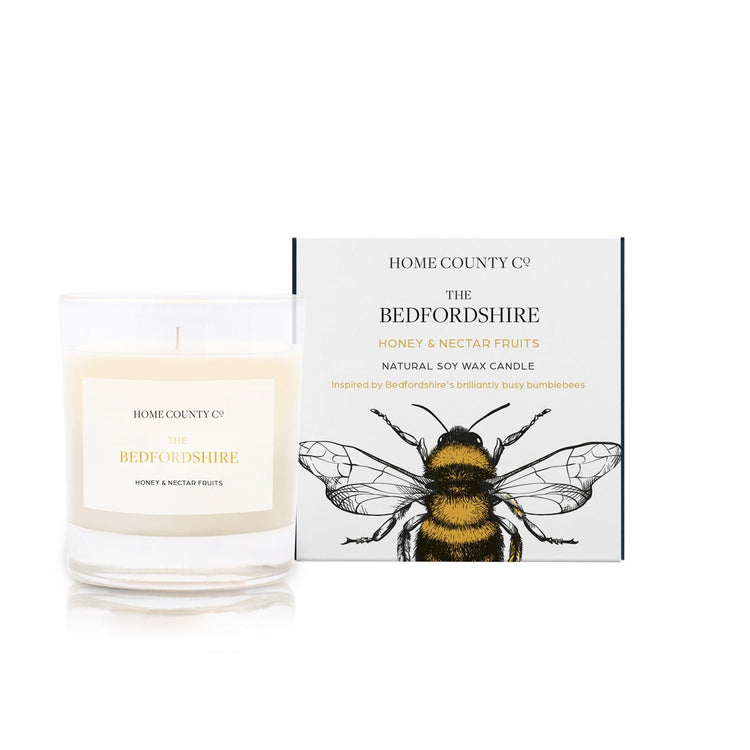A honey and nectar fruits scented candle from Home County Co. The cotton wick soy candle is shown next to the eco friendly candle box packaging.