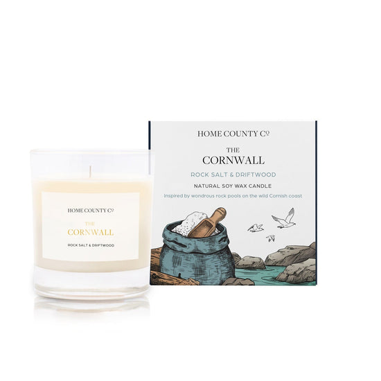 A rock salt and driftwood scented candle from Home County Co. The cotton wick soy candle is shown next to the eco friendly candle box packaging.