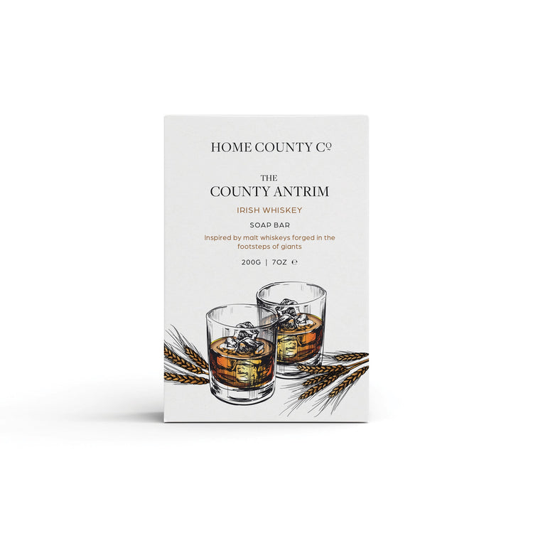 An Irish Whiskey scented natural soap bar from the Home County Co. is shown in its whiskey illustrated recyclable soap bar wrap