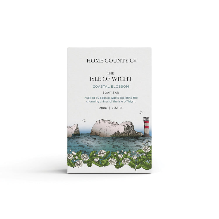 A coastal blossom scented natural soap bar from the Home County Co. is shown in its Isle of Wight needles illustrated recyclable soap bar wrap