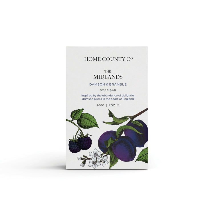 A plum scented natural soap bar from the Home County Co. is shown in its plum illustrated recyclable soap bar wrap