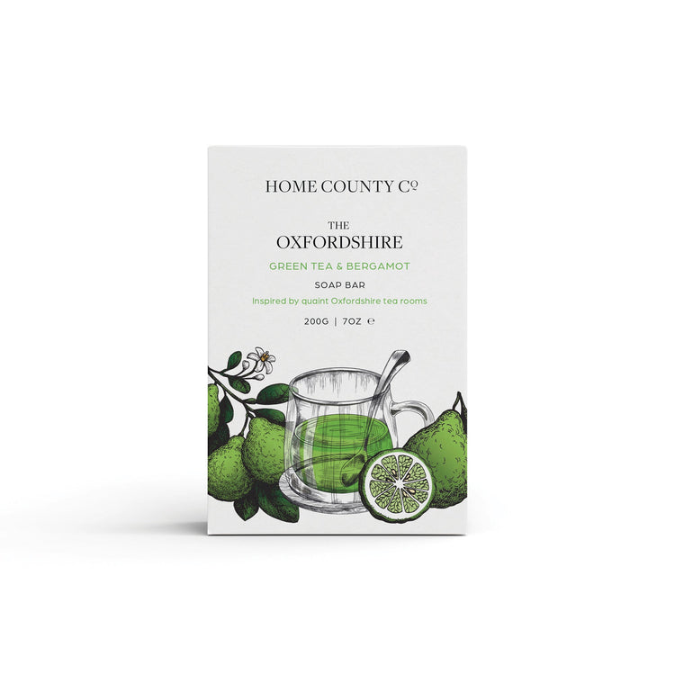 A green tea scented natural soap bar from the Home County Co. is shown in its green tea and bergamot illustrated recyclable soap bar wrap