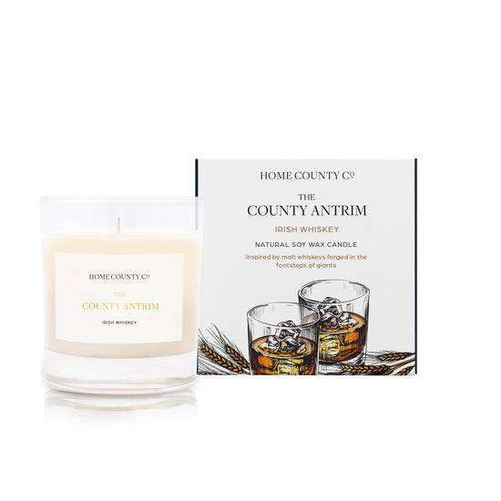 An Irish whiskey scented candle from Home County Co. The cotton wick soy candle is shown next to the eco friendly box packaging.