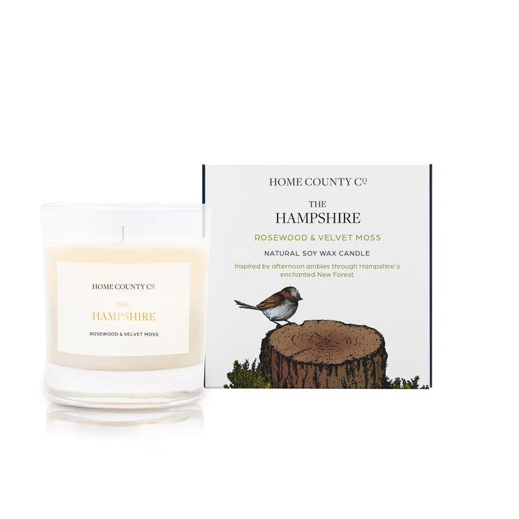 A rosewood and velvet moss scented candle from Home County Co. The cotton wick soy candle is shown next to the eco friendly candle box packaging.