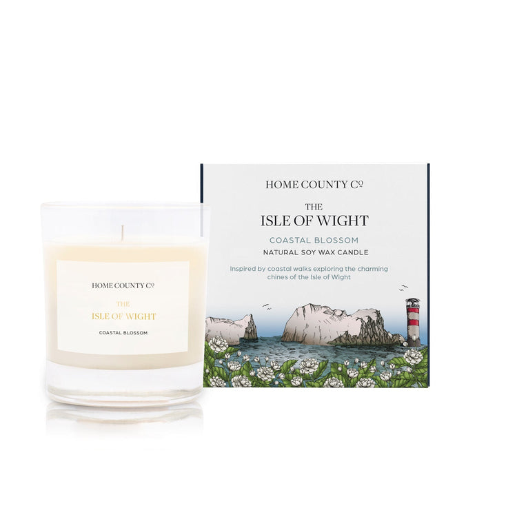 A coastal blossom scented candle from Home County Co. The cotton wick soy candle is shown next to the eco friendly candle box packaging which displays an illustration of the Isle of Wight coast and lighthouse.