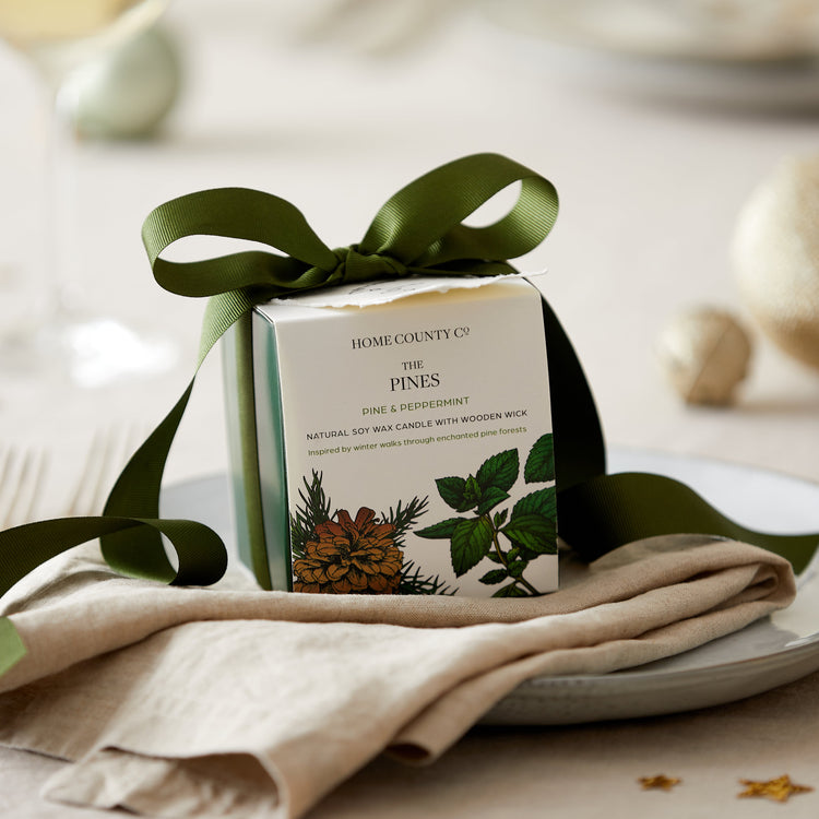 A pine and peppermint scented candle from the Home County Co. is shown alight on a Christmas table