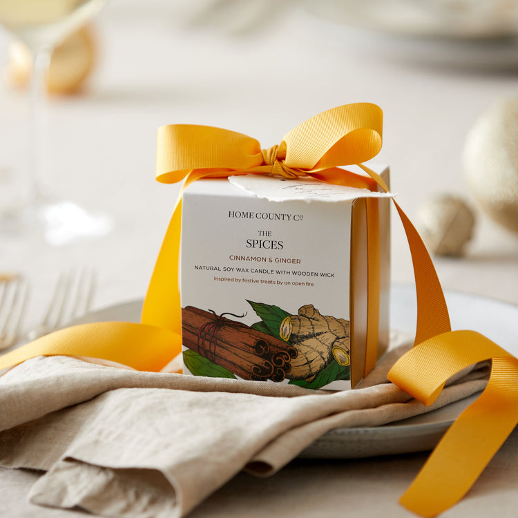 A cinnamon and ginger scented candle from the Home County Co. is shown alight on a Christmas table