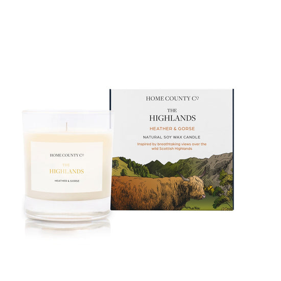 A Scottish Highlands candle from the Home County Co is shown next to the Highland Cow illustrated candle box