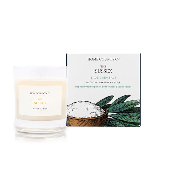 A sage and sea salt scented candle from Home County Co. The cotton wick soy candle is shown next to the eco friendly candle box packaging.