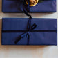 A Christmas candle gift set from the Home County Co. is shown with luxury Gift Wrap. The gift set is wrapped in luxury navy wrapping paper secured with navy ribbon.