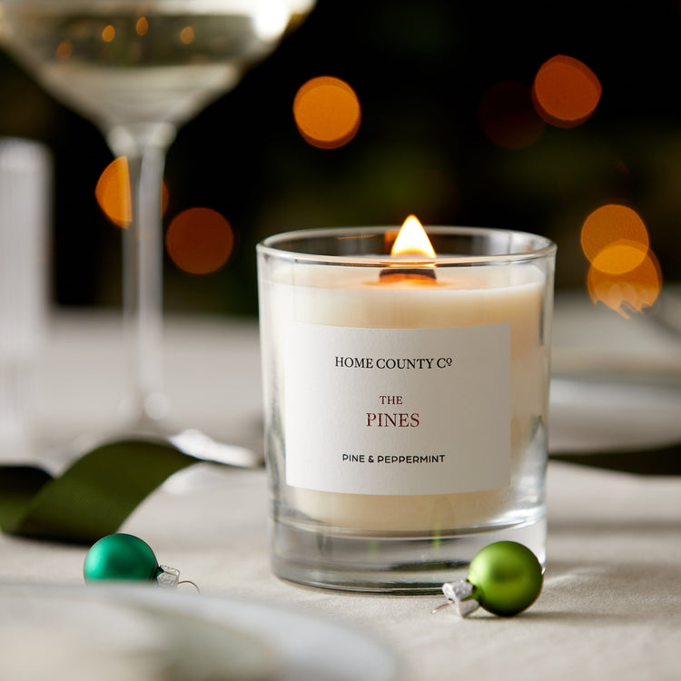 A pine and peppermint scented candle from the Home County Co. is shown alight on a Christmas table 