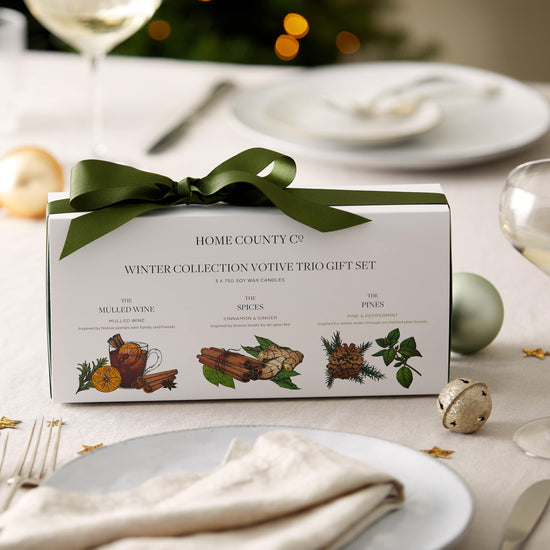 Three votive Christmas candles from the Home County Co are shown alight on a Christmas themed table