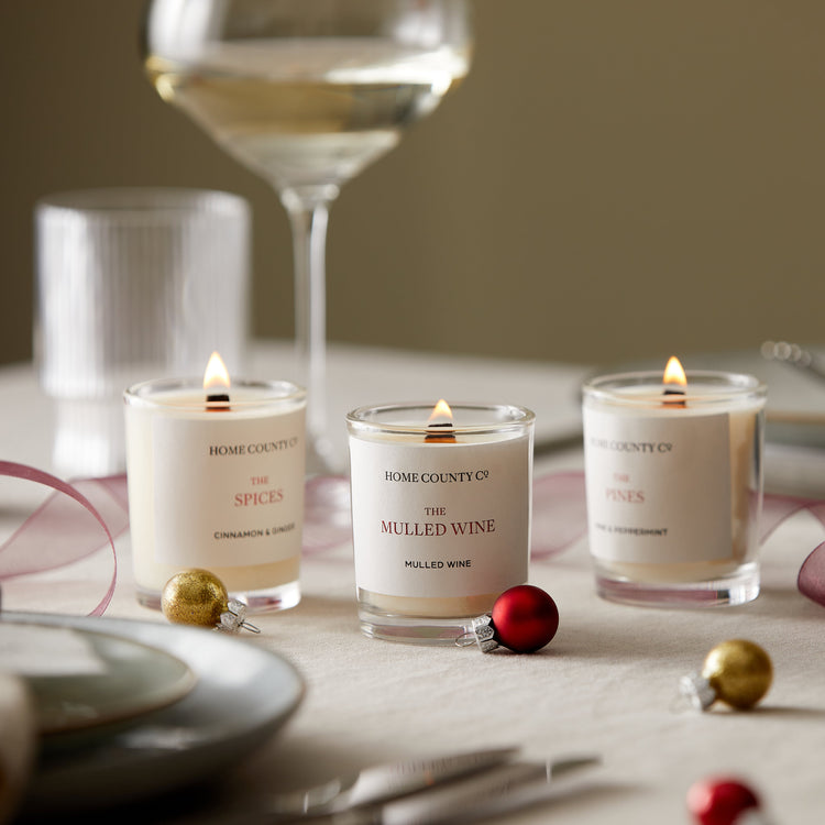 Three votive Christmas candles from the Home County Co are shown alight on a Christmas themed table